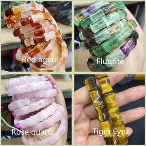Op de afbeelding: Vier armbanden gemaakt van natuurlijke edelstenen: rode agaat, fluoriet, rozenkwarts en tijgeroog. De armbanden zijn gemaakt van cilindrische kralen die aan elkaar zijn geregen. De tekst "Red agate", "Fluorite", "Rose quartz" en "Tiger Eyes" is zichtbaar.