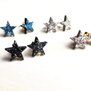 Op de afbeelding: Zes paar stervormige oorbellen in zwart, zilver en blauw glitter. De oorbellen zijn klein en delicaat.