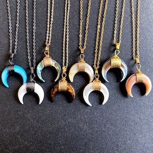 May include: A set of eight gold-toned necklaces with crescent moon pendants made of different types of shell. The pendants are wrapped with gold wire.