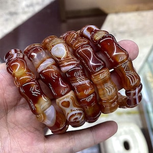 Op de afbeelding: Een verzameling gepolijste agaatarmbanden. De armbanden hebben een mix van roodbruine en witte banden, met een glanzende afwerking. De cilindrische kralen zijn geregen en tonen natuurlijke patronen.