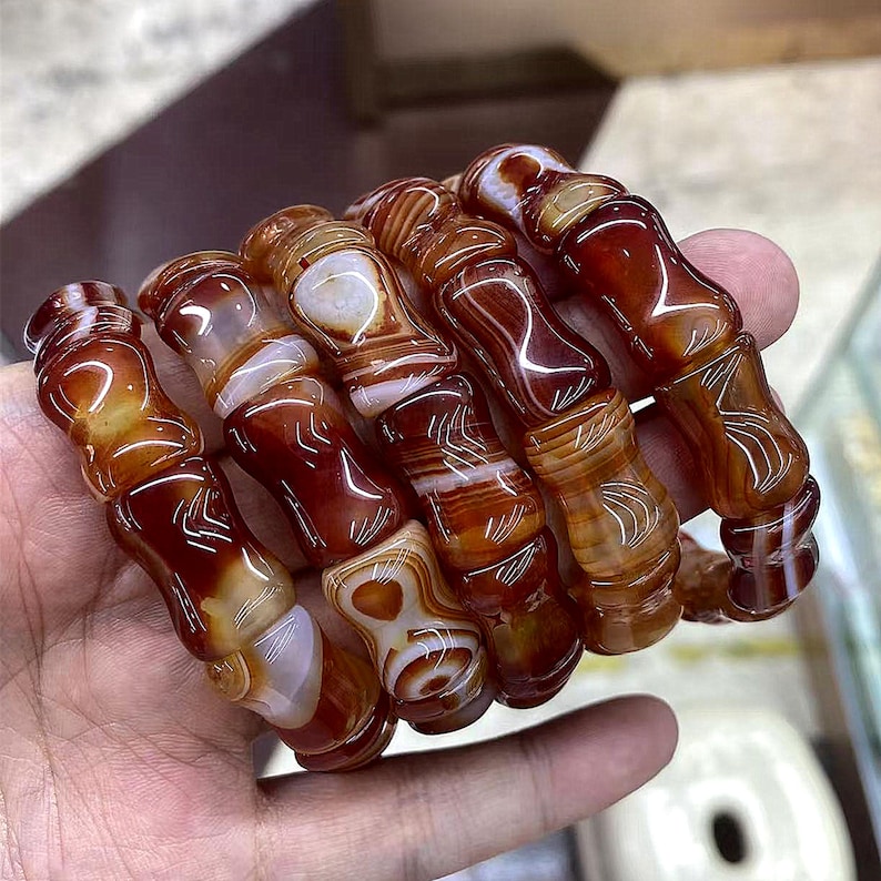 Op de afbeelding: Een verzameling gepolijste agaatarmbanden. De armbanden hebben een mix van roodbruine en witte banden, met een glanzende afwerking. De cilindrische kralen zijn geregen en tonen natuurlijke patronen.