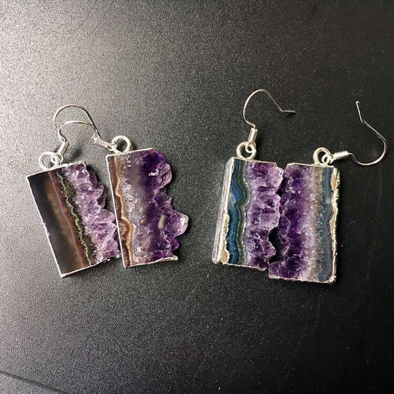 Puede incluir: Un par de pendientes de plata con detalles de cristal de amatista. Los cristales son de color morado intenso y tienen una textura natural y rugosa. Los pendientes son un accesorio &uacute;nico y elegante.