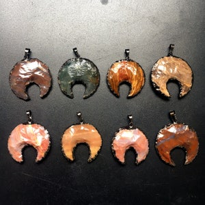 May include: Eight crescent moon shaped pendants made of agate with a black metal bail. The pendants are in various colors including brown, orange, pink, and green.