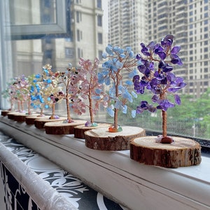 May include: A row of ten small crystal trees on wooden bases. The trees are made of wire and various coloured crystals. The trees are arranged in a line from left to right, with the smallest tree on the left and the largest tree on the right.
