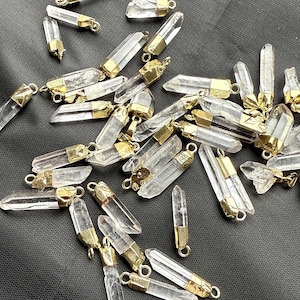 May include: A collection of clear quartz crystal pendants with gold-toned metal caps. The crystals are various sizes and shapes, and the caps have a smooth, polished finish.