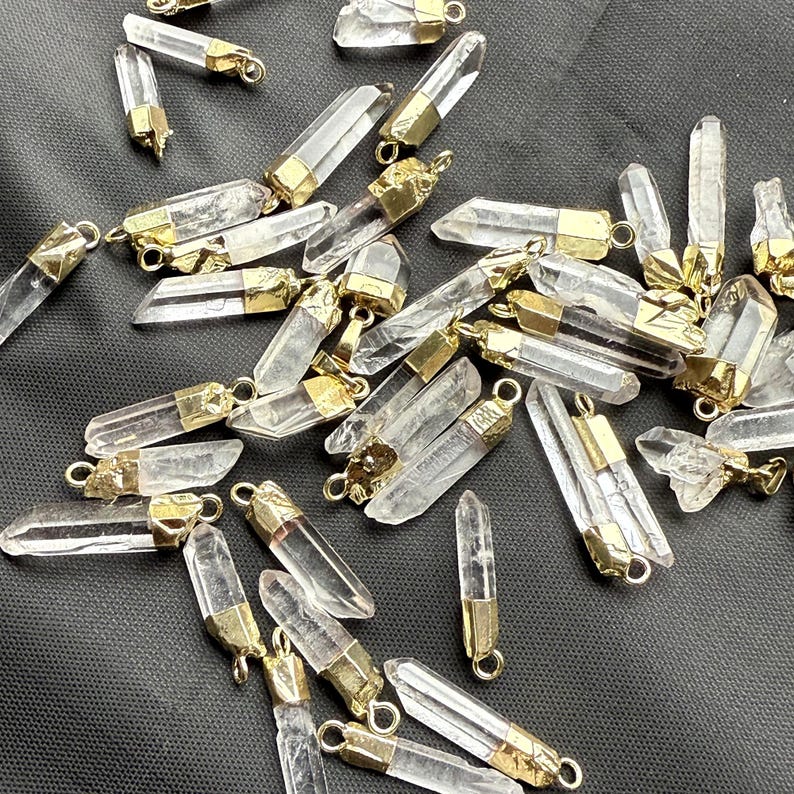 May include: A collection of clear quartz crystal pendants with gold-toned metal caps. The crystals are various sizes and shapes, and the caps have a smooth, polished finish.