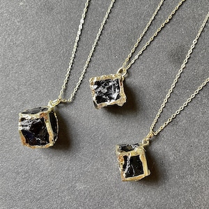 May include: Three gold necklaces with black stone pendants. Each pendant is a different shape and size, but all have a gold frame.