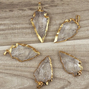May include: Five clear quartz arrowhead pendants with gold rims. The arrowheads are all different sizes and shapes, but they all have a similar pointed tip and a flat base. The pendants are ideal for making jewellery or adding a touch of natural beauty to any project.