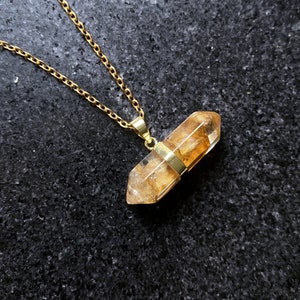 May include: A gold chain necklace with a clear quartz crystal pendant. The crystal is faceted and has a golden hue.