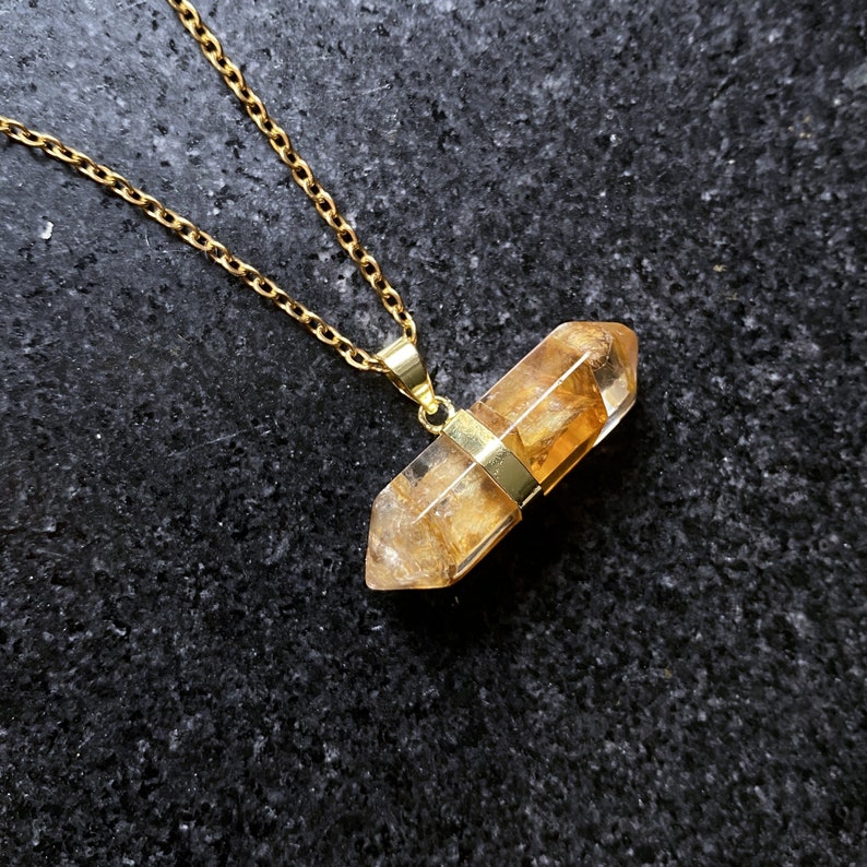 May include: A gold chain necklace with a clear quartz crystal pendant. The crystal is faceted and has a golden hue.