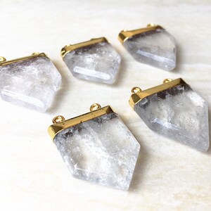 Puede incluir: Cinco colgantes de cristal de cuarzo transparente con tapas y lazos de metal dorado. Los cristales son facetados y tienen una textura natural rugosa.