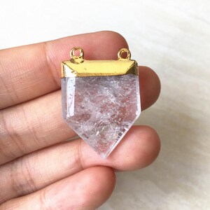 Puede incluir: Un colgante de cristal de cuarzo transparente con una parte superior chapada en oro y dos anillos de salto. El cristal est&aacute; facetado y tiene una punta puntiaguda.