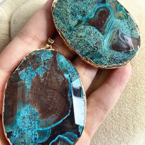 May include: Two oval-shaped agate pendants with gold-toned metal accents. The agate is a deep blue-green with brown and black swirls and patterns.