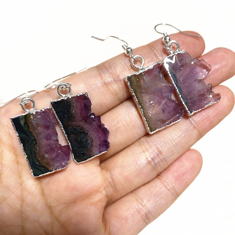 Puede incluir: Un par de pendientes de plata con piedras de cristal de amatista p&uacute;rpura y negra. Las piedras est&aacute;n engastadas en un marco de plata y tienen una forma natural irregular.