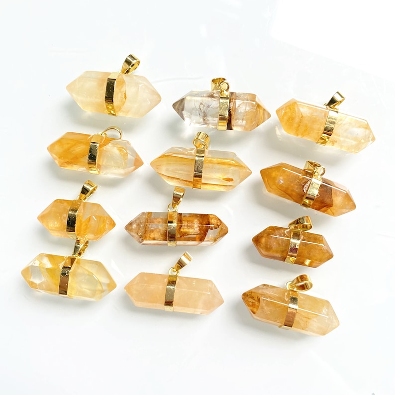 May include: Twelve gold-capped, clear quartz crystal pendants with a golden brown hue. The pendants are in the shape of double-ended points.