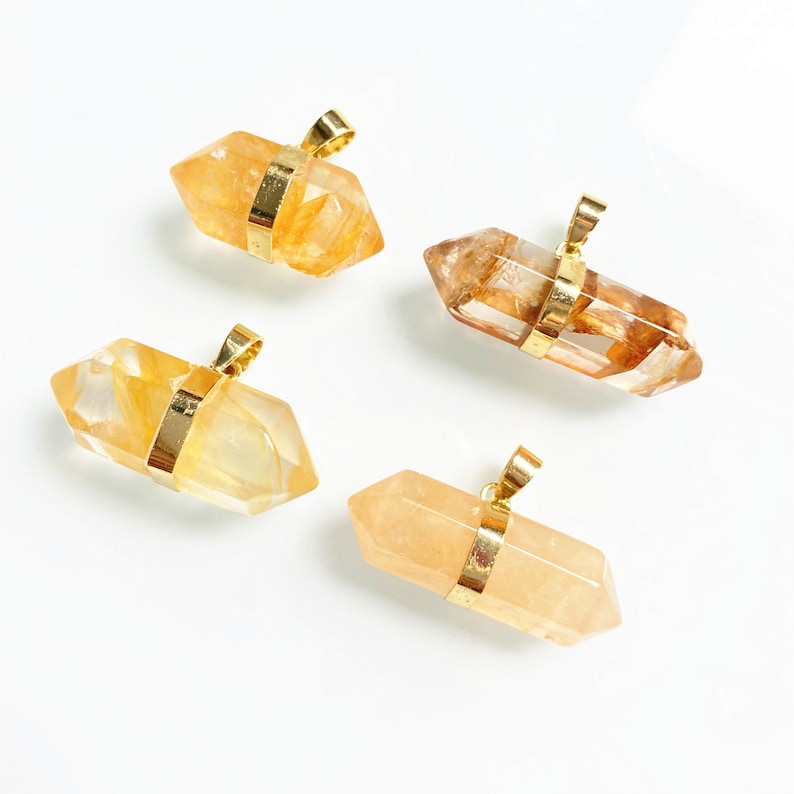 May include: Four gold-wrapped crystal pendants in various shades of yellow and orange. The pendants are shaped like double-ended points and have a gold bail for hanging.