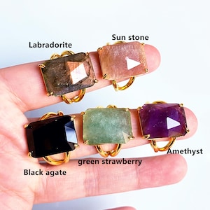 May include: Five gold rings with different coloured gemstones. The rings feature a square-shaped stone with a faceted design. The stones are labradorite, sunstone, green strawberry, amethyst, and black agate.