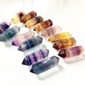May include: A collection of ten double-pointed fluorite crystal wands in various shades of purple, blue, yellow, and green.