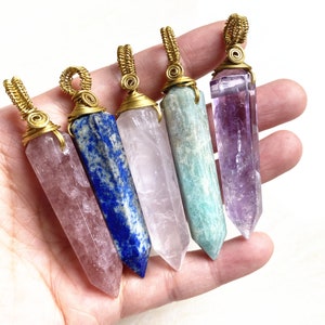Könnte beinhalten: Fünf Kristallspitzen-Anhänger, die in goldenen Draht gewickelt sind. Die Kristalle sind Amethyst, Rosenquarz, klarer Quarz, Aquamarin und Lapislazuli.