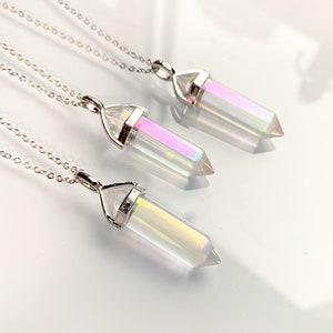 Puede incluir: Tres collares de plata con colgantes de cristal transparente iridiscente. Los collares están superpuestos sobre una superficie blanca.