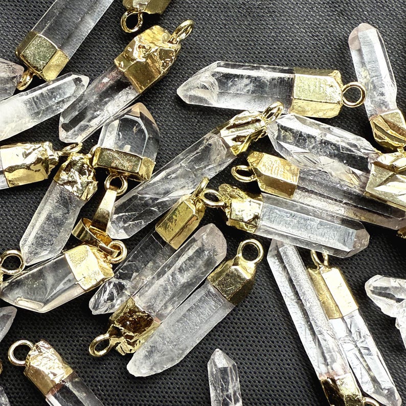 May include: A collection of clear quartz crystal pendants with gold-toned metal caps. The crystals are faceted and have a pointed tip. The pendants are perfect for jewelry making or crafting.