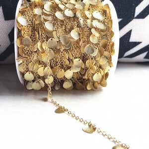 May include: A spool of gold chain with small, round, scalloped metal charms. The chain is coiled and the charms hang down from the chain.