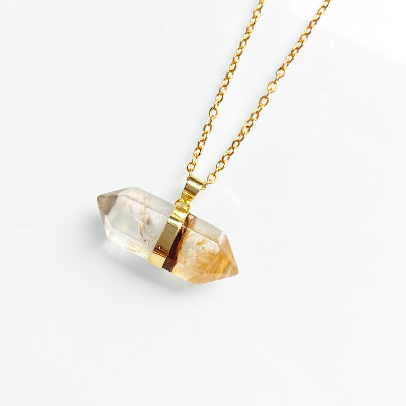 May include: A gold chain necklace with a clear quartz crystal pendant. The crystal is faceted and has a gold band around the middle.