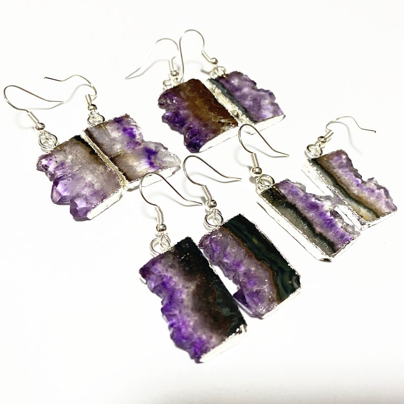 Puede incluir: Cuatro pares de pendientes colgantes de plata con piedras de cristal de amatista. Los cristales son de color morado intenso con un borde natural en bruto. Los pendientes son un accesorio &uacute;nico y elegante.