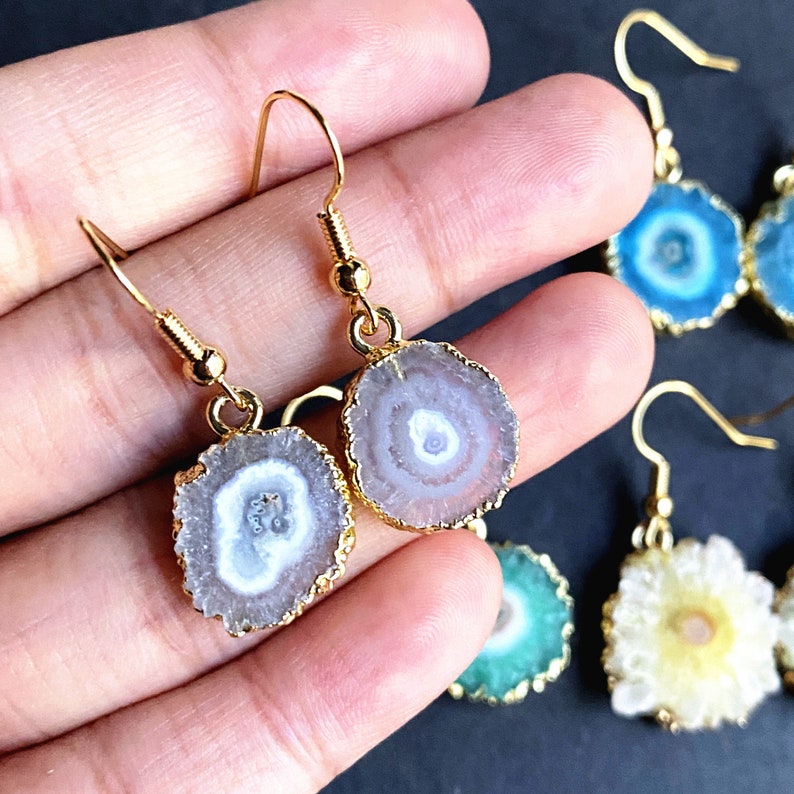 Puede incluir: Un par de pendientes de tono dorado con una piedra de &aacute;gata blanca y rosa. Las piedras son redondas y tienen un aspecto natural y org&aacute;nico. Los pendientes son un accesorio delicado y femenino.