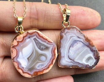 May include: Two agate stone pendants with gold-toned chain necklaces. The pendants are both irregularly shaped and feature a white and brown agate pattern with a reddish-brown border.