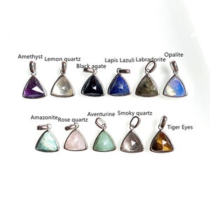 Puede incluir: Un conjunto de 10 colgantes de piedras preciosas en forma de triángulo con engastes de plata. Las piedras son amatista, cuarzo limón, ágata negra, lapislázuli, labradorita, ópalo, amazonita, cuarzo rosa, aventurina y cuarzo ahumado.