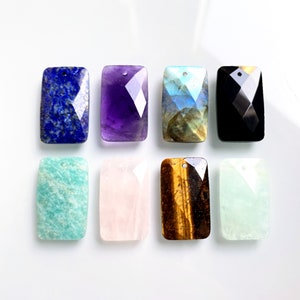 Może przedstawiać: Osiem prostokątnych zawieszek z kamieni szlachetnych o fasetowanych krawędziach i otworem na górze do nawlekania. Kamienie to ametyst, czarny onyks, awenturyn, labradoryt, różowy kwarc, tygrysie oko i dwa odcienie zieleni.