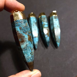 May include: Four turquoise and brown agate gemstone pendants with gold-toned tops. The pendants are shaped like long, narrow points.