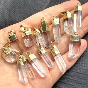May include: A collection of 12 clear quartz crystal point pendants with gold-plated caps. The pendants are various sizes and shapes, and they are all strung on a gold chain.