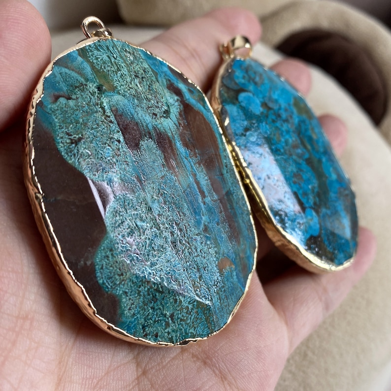 May include: Two agate pendants with gold-plated edges. The pendants are oval-shaped and feature a blue and brown marbled pattern.