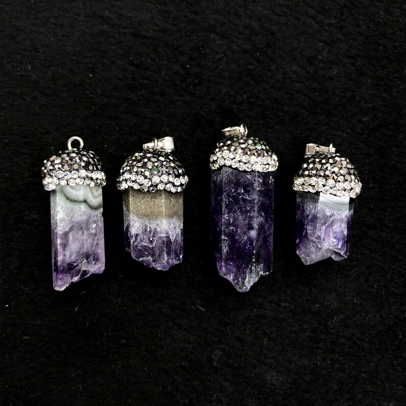 Puede incluir: Cuatro colgantes de cristal de amatista con engastes plateados y diamantes de imitaci&oacute;n transparentes. Los colgantes son de diferentes tama&ntilde;os y tienen una gama de colores p&uacute;rpura y blanco.
