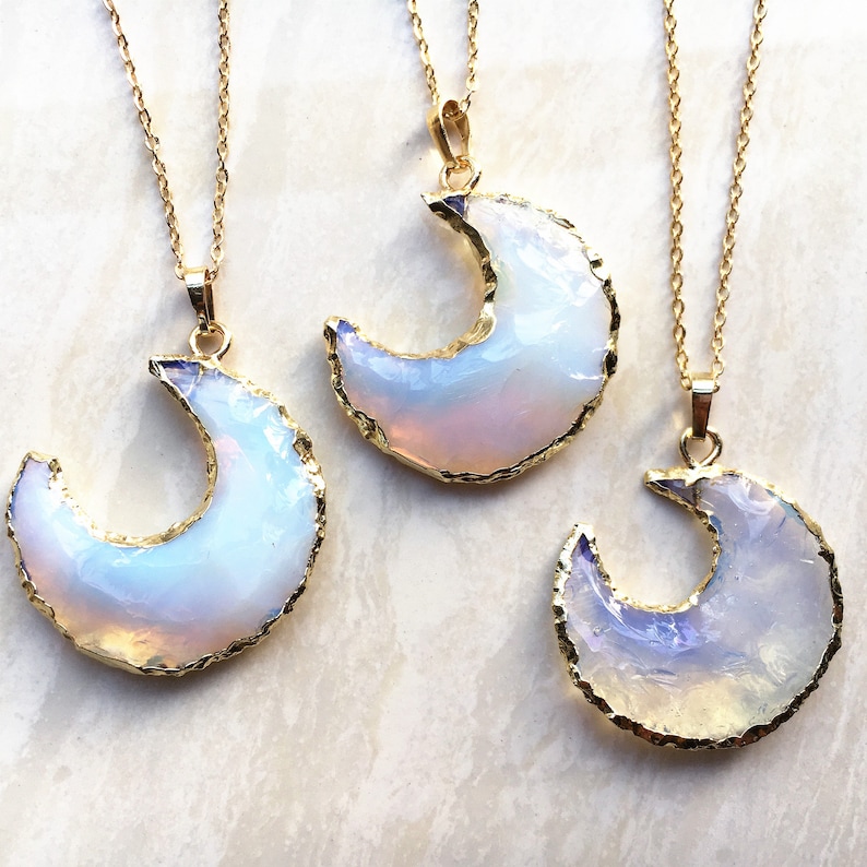 May include: Three gold necklaces with iridescent opal crescent moon pendants. The necklaces are on a white background.