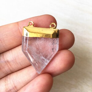 Puede incluir: Un colgante de cristal de cuarzo transparente con una parte superior chapada en oro y dos bucles para sujetar una cadena. El cristal tiene forma de punta y un dise&ntilde;o facetado.