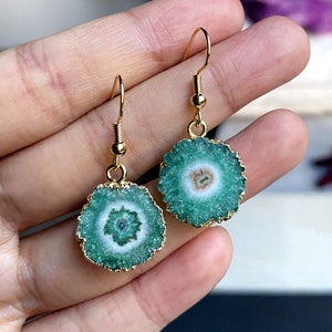 Puede incluir: Un par de pendientes de oro con detalles de piedra de &aacute;gata verde. Los pendientes presentan una piedra redonda verde con un centro blanco y un bucle de alambre dorado.