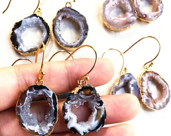 May include: A pair of gold-toned earrings with agate stone accents. The earrings feature a round, hollowed-out agate stone with a white and gray interior and a black exterior. The agate stones are attached to gold-toned hooks.