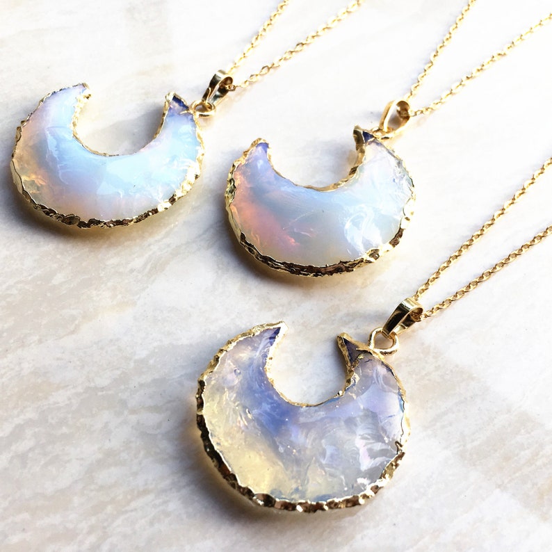 May include: Three gold necklaces with opal crescent moon pendants. The opals are iridescent and have a white, blue, and pink color.