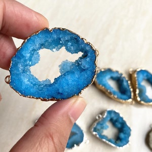 May include: A blue agate pendant with a gold-plated edge. The agate has a natural hole in the center, creating a unique and eye-catching design.