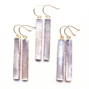 May include: Three pairs of gold earrings with selenite crystal pendants. The selenite crystals are long and rectangular, with a white, translucent colour.