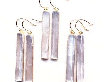 Puede incluir: Tres pares de pendientes de oro con colgantes de cristal de selenita. Los cristales de selenita son largos y rectangulares, de color blanco translúcido.