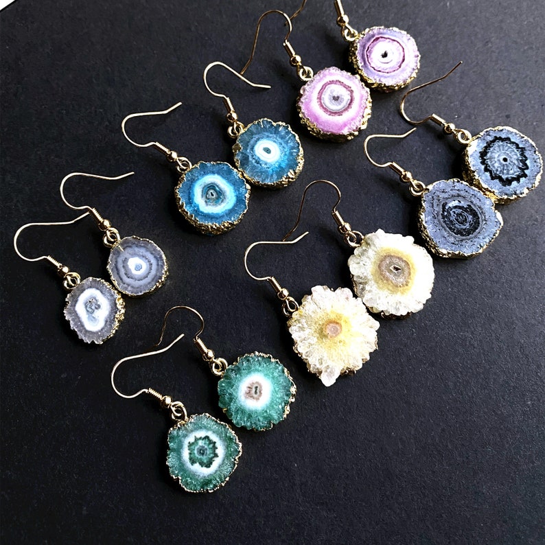 Puede incluir: Un conjunto de diez pendientes de oro con diferentes rebanadas de &aacute;gata de colores. Cada pendiente presenta un patr&oacute;n y un color &uacute;nicos, incluyendo rosa, azul, verde y blanco.