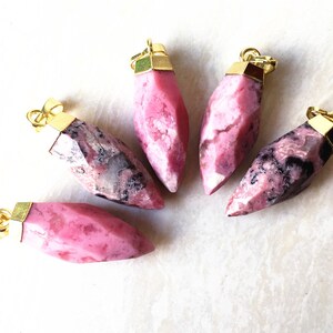 Puede incluir: Cinco colgantes de piedra rosa y negra con tapas de metal dorado. Los colgantes tienen forma de lágrima puntiaguda.