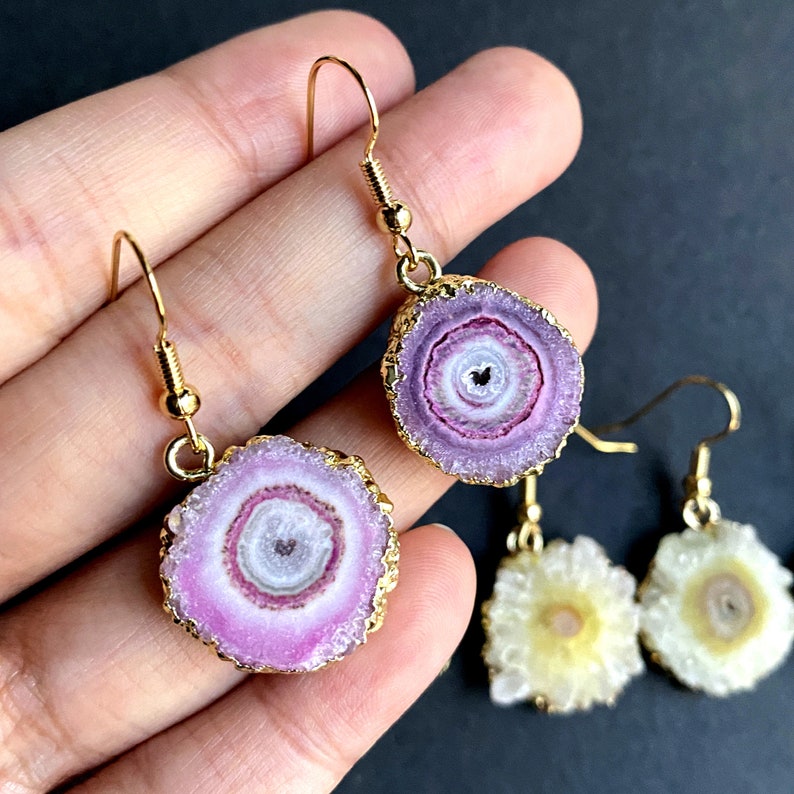 Puede incluir: Un par de pendientes de oro con rodajas de &aacute;gata rosa y blanca. Las rodajas de &aacute;gata tienen una forma circular con anillos conc&eacute;ntricos de color. Los pendientes cuelgan de ganchos de oro.