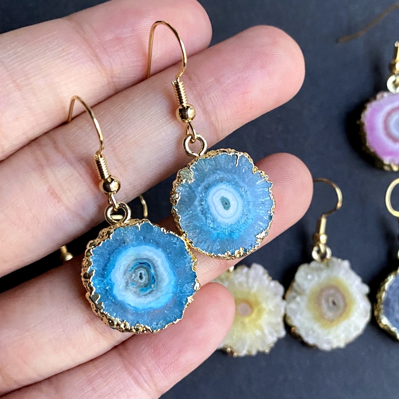 Puede incluir: Un par de pendientes de oro con detalles de piedra de &aacute;gata azul. Los pendientes son redondos y tienen un borde dorado. Las piedras de &aacute;gata tienen un centro blanco y un anillo exterior azul.