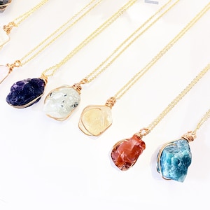 May include: Seven gold necklaces with different coloured natural crystal pendants. The crystals are wrapped in gold wire and include amethyst, clear quartz, citrine, carnelian, and green aventurine.