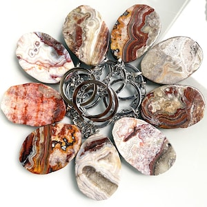 May include: A set of nine agate slices with red, brown, and white patterns, attached to a silver key ring. The agate slices are all different shapes and sizes.